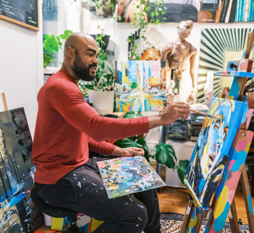 A man painting a colorful portrait in a brightly lit art studio.