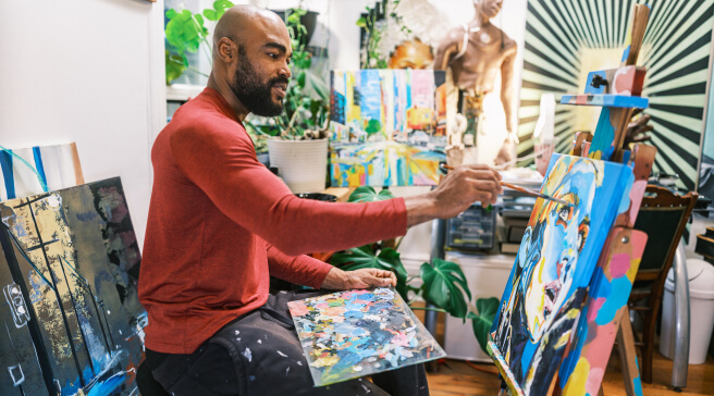 A man painting a colorful portrait in a brightly lit art studio.