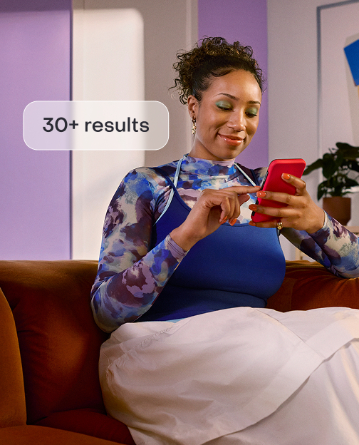 A woman sitting on a couch browsing housing listings on the Zillow app.