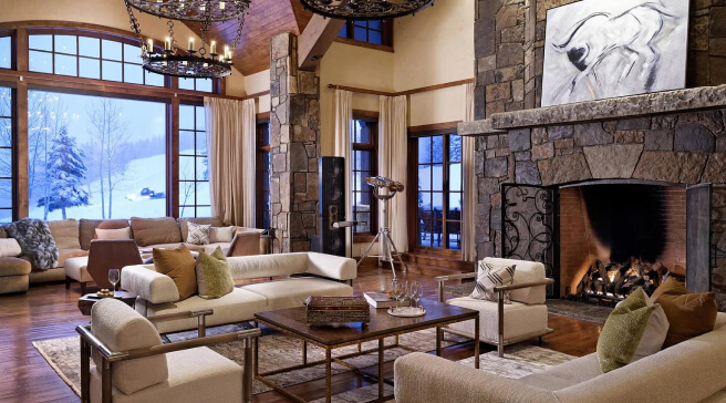 Spacious living room with a large stone fireplace and snowy views outside.